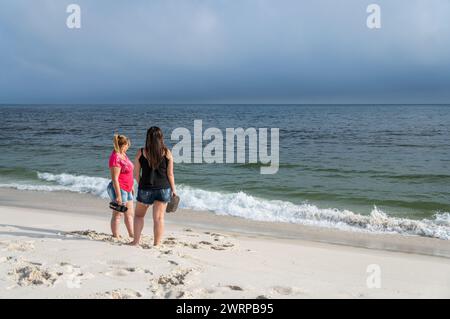 Two woman standing and looking at the sea on the empty Praia Seca beach sands close to Sao Judas Tadeu street under summer afternoon clouded sky. Stock Photo