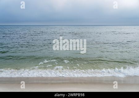 Calm waves from Atlantic Ocean blue waters hitting and washing the white sands of Praia Seca beach under summer afternoon clouded sky. Stock Photo