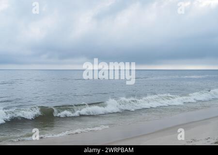 Gentle ocean waves from Atlantic Ocean blue waters breaking and hitting the white sands at Praia Seca beach under summer afternoon clouded sky. Stock Photo
