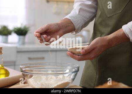 Making bread. Man putting dry yeast into bowl with flour at wooden table in kitchen, closeup Stock Photo