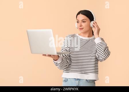 Female programmer in headphones with laptop on beige background Stock Photo