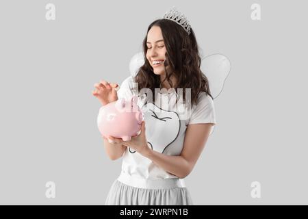Tooth Fairy putting coin into piggy bank on light background Stock Photo