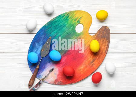 Paint palette and Easter eggs on wooden white background. Easter concept. Stock Photo