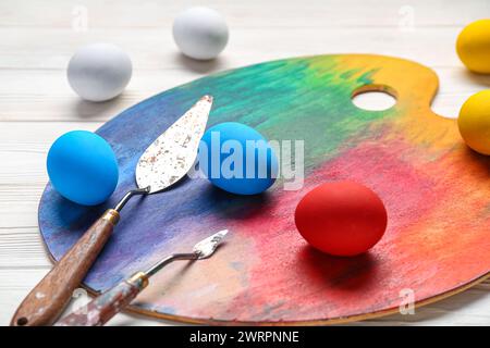 Rainbow paint palette and Easter eggs on wooden white background, closeup. Stock Photo