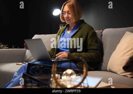Female nurse with laptop on sofa working evening shift in clinic Stock Photo