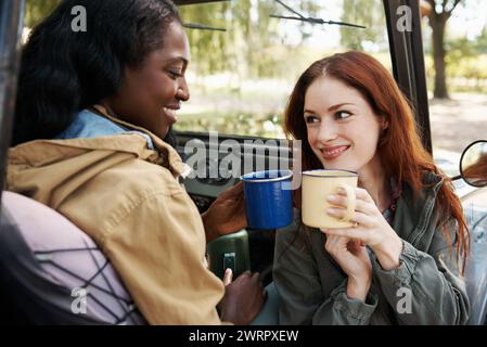 Women, coffee or relax on road trip in countryside, talking or travel adventure as friends in nature. Ladies, drinking and tea in suv on summer Stock Photo