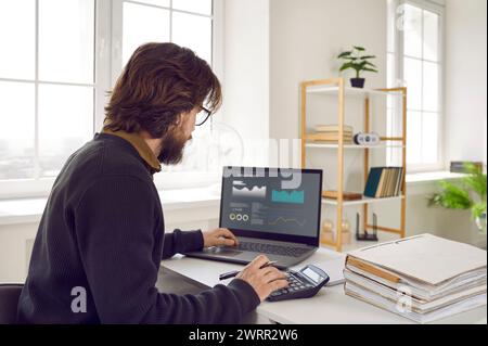 Man sitting at office desk, using laptop computer and working with financial data Stock Photo