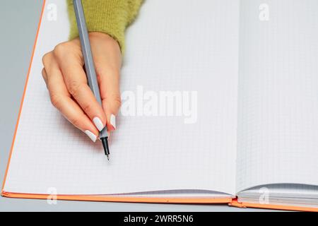 Close-up of a woman's hand writing in a checkered notebook with a gray pen Stock Photo
