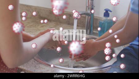 Image of coronavirus cells over caucasian mother with son washing hands at home Stock Photo