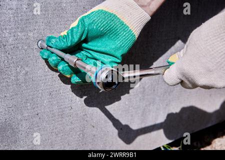 Finishing plinth on stilts with flat slate, worker uses socket wrench to tighten mounting screw. Stock Photo