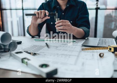 Engineering hands hold vernier caliper working and checking joint pipe scale with drawings inspection on the office desk and Calculator, triangle rule Stock Photo