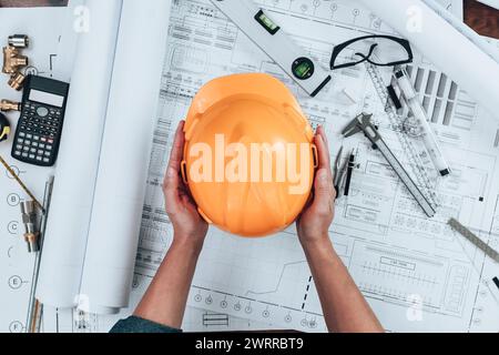 Engineering holding safety helmet  with drawings inspection on the office desk and Calculator, triangle ruler, safety glasses, compass, vernier calipe Stock Photo