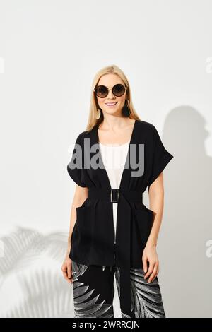 Studio portrait of a woman in black sleeveless shirt with belt, blouse and floral-patterned trousers Stock Photo