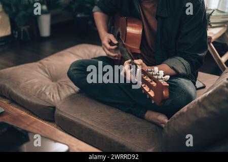 young man relax and playing guitar while sitting on sofa bed in living room at home. Music hobby and practice concept. Stock Photo