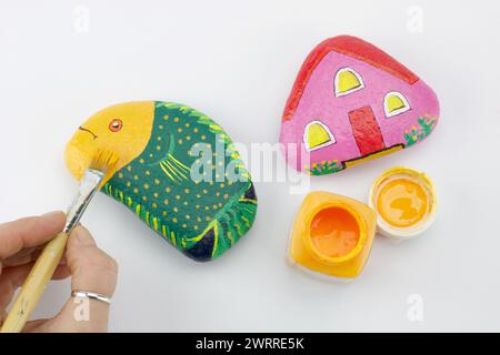 hand with brush painting multicolored stones isolated on white background Stock Photo