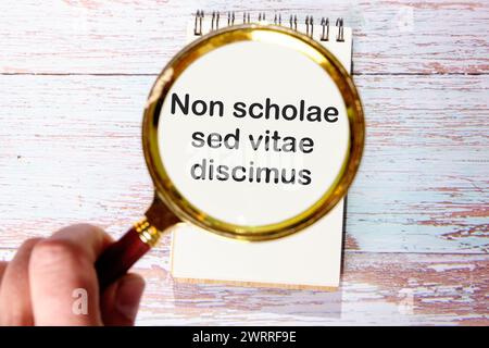 Non scholae sed vitae discimus It is translated from Latin as We study not for school, but for life. through a magnifying glass on a notebook Stock Photo