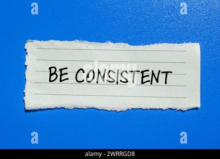 Be consistent words written on torn paper with blue background. Conceptual symbol. Copy space. Stock Photo