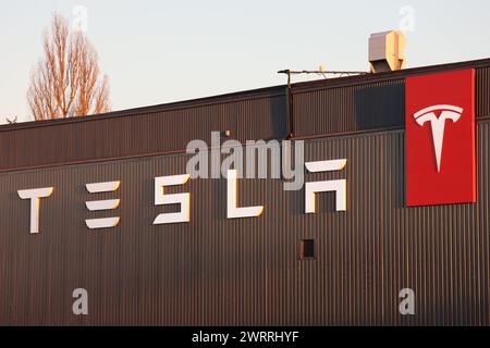 Tesla's new font in white on a brown house wall with a red Tesla badge. Blue sky at the top of the image Stock Photo