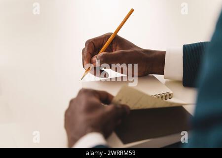 Close-up on note-taking: businessman's hands writing in a notepad during a corporate meeting - focus on effective note-taking. Stock Photo