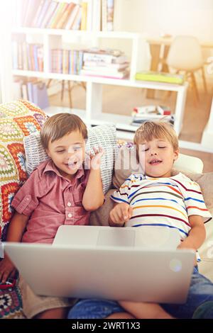 Children, laptop and siblings on a sofa with cartoon, film or streaming movie at home. Computer, learning and boy kids in a house for google it Stock Photo