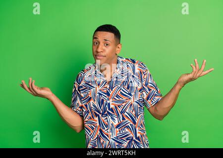 Photo of attractive puzzled man wear stylish clothes raise hands excuse me sorry isolated on green color background Stock Photo