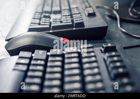 Mouse with red scrolling wheel between keyboards on office desk Stock Photo