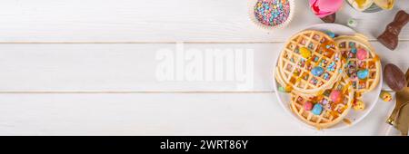 Easter breakfast or brunch. Cute creative decor portion of soft sweet belgian waffles with Easter chocolate eggs, sugar sprinkles and jam or syrup dri Stock Photo