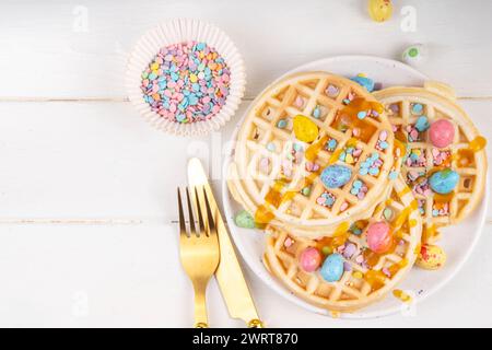 Easter breakfast or brunch. Cute creative decor portion of soft sweet belgian waffles with Easter chocolate eggs, sugar sprinkles and jam or syrup dri Stock Photo