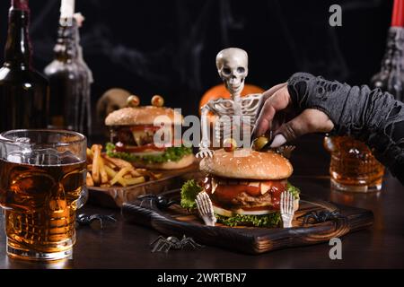 The witches hand holds the eye of Monstera Burger on a sitting skeleton. Perfect Halloween Party appetizer Stock Photo