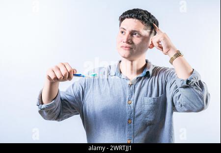 Pensive man holding toothbrush isolated. Thoughtful person holding toothbrush and looking up isolated Stock Photo