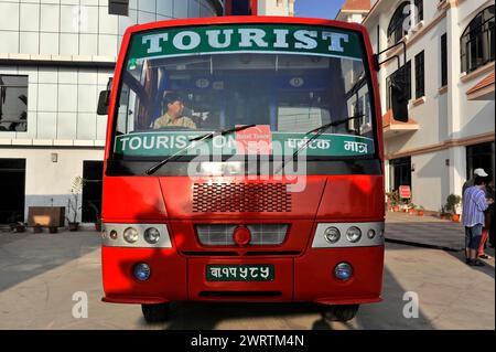 A red tourist bus stands in front of a light-coloured building, Bhairahawa, Nepal Stock Photo