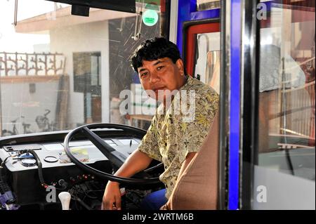 A smiling bus driver sits relaxed in the driver's compartment of a bus, Bhairahawa, Nepal Stock Photo