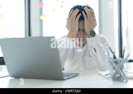 Young businessman sitting at his desk looking at the internet on his laptop Feeling stressed, anxious, unhappy in the office. Stock Photo
