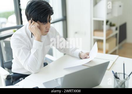 Young businessman sitting at his desk looking at the internet on his laptop Feeling stressed, anxious, unhappy in the office. Stock Photo
