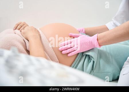 Qualified gynecologist-obstetrician in medical gloves examining belly of woman on second trimester of pregnancy, checking the presentation of baby Stock Photo