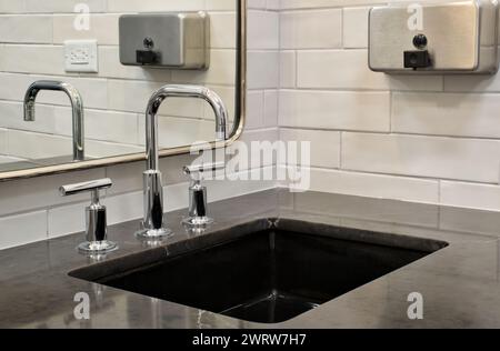 Bathroom sink vanity design with black marble countertop, mirror and soap dispenser, low angle view. Stock Photo