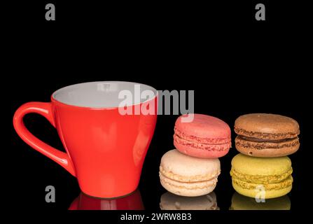 Several sweet macarons with a ceramic red cup, macro, isolated on black background. Stock Photo