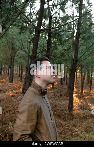 Stock photo of a young man looking around in the forest enjoying nature surrounded by trees Stock Photo