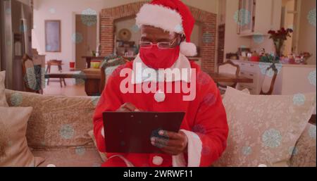 Image of snow falling over man wearing santa claus costume and face mask with clipboard Stock Photo