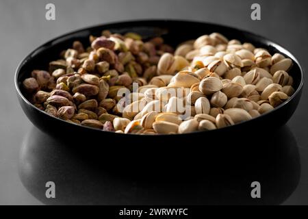 Peeled and unpeeled pistachios in a black plate on a dark background. Healthy products, snacks for beer. Stock Photo