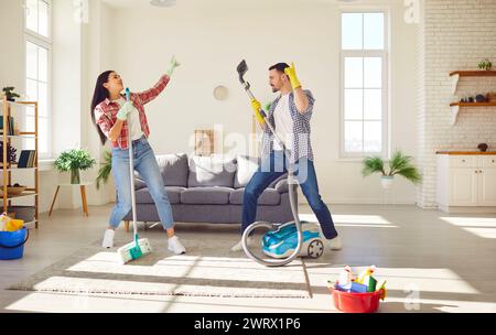 Funny couple cleaning home together having fun, dancing at home while housekeeping work Stock Photo