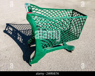 Green shopping cart fabricated from recycled plastic outdoors on asphalt with sunlight shade Stock Photo
