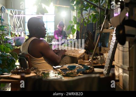 Selective focus shot of African American hacker coding on old desktop computer in post-apocalyptic house Stock Photo