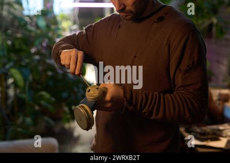 Medium crop shot of man wearing shabby clothes repairing old air-purifying respirator using screwdriver, post-apocalypse concept Stock Photo