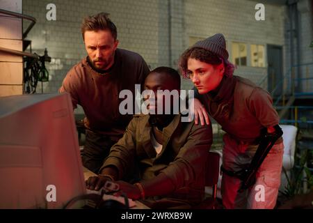 Group of three diverse scientists surviving apocalypse working with data on old computer in abandoned factory Stock Photo