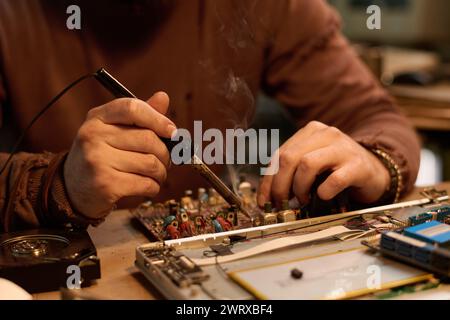 Closeup of hands of unrecognizable technician repairing old electronic device using soldering iron Stock Photo
