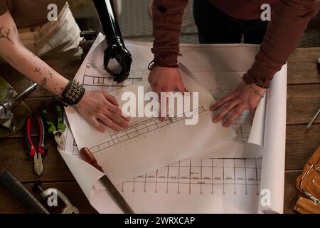 From above view shot of unrecognizable male and female technicians standing at wooden table working with technical drawings, salvagepunk aesthetics Stock Photo
