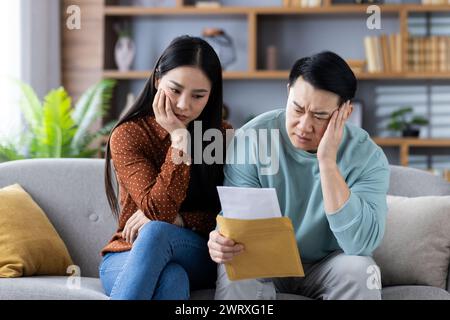A man and woman sitting on a sofa reviewing documents with a worried expression, depicting financial or domestic issues. Stock Photo