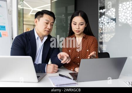 Two focused business colleagues working together on a laptop, engaged in a project discussion inside a modern office. Stock Photo