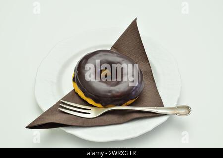 chocolate donut on white plate with brown napkin, close up, isolated on white background Stock Photo